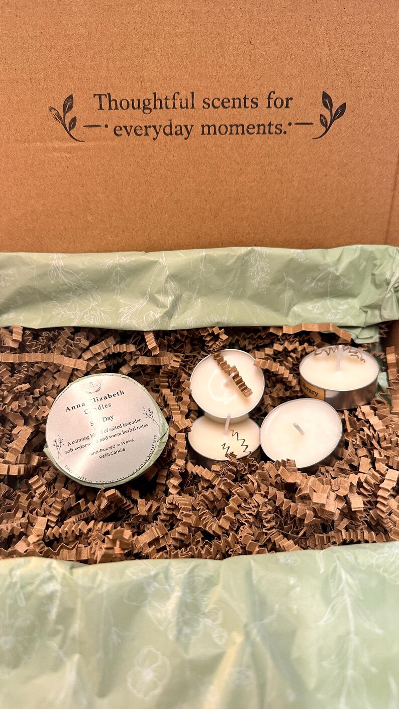 May include: A gift box with candles and decorative paper. The box is brown with the text "Thoughtful scents for everyday moments." Inside are several small, round candles in metal holders, and a round candle with a label. The box is filled with brown paper.