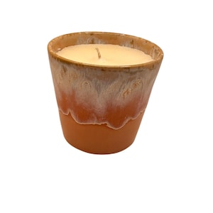 May include: A candle in a ceramic container. The container is a warm terracotta colour at the base, transitioning to a creamy white at the top. The candle itself is a light beige colour with a single wick.