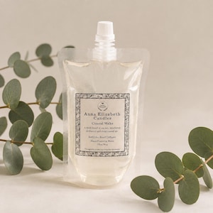 May include: A clear plastic refill pouch for a reed diffuser by Anna Elizabeth Candles, labelled Coastal Walks. The label describes a blend of sea salt, driftwood, and coastal air, noting it is hand-poured in Wales using olive wax for home fragrance.