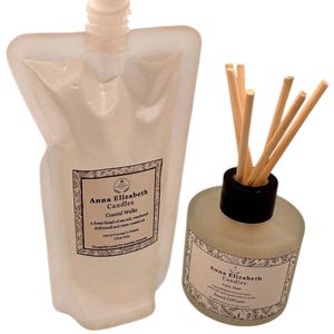 May include: A clear pouch and a glass bottle with reed diffuser sticks. Both feature labels with the text "Anna Elizabeth Candles" and "Coastal Walks" and "Fairy Dust". The pouch has a white cap.