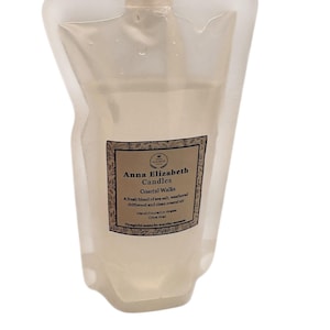 May include: A clear, flexible pouch with a white cap, containing a liquid. The label reads "Anna Elizabeth Candles Coastal Walks" with a description of the scent. The product is hand-poured in Wales and made with olive wax.