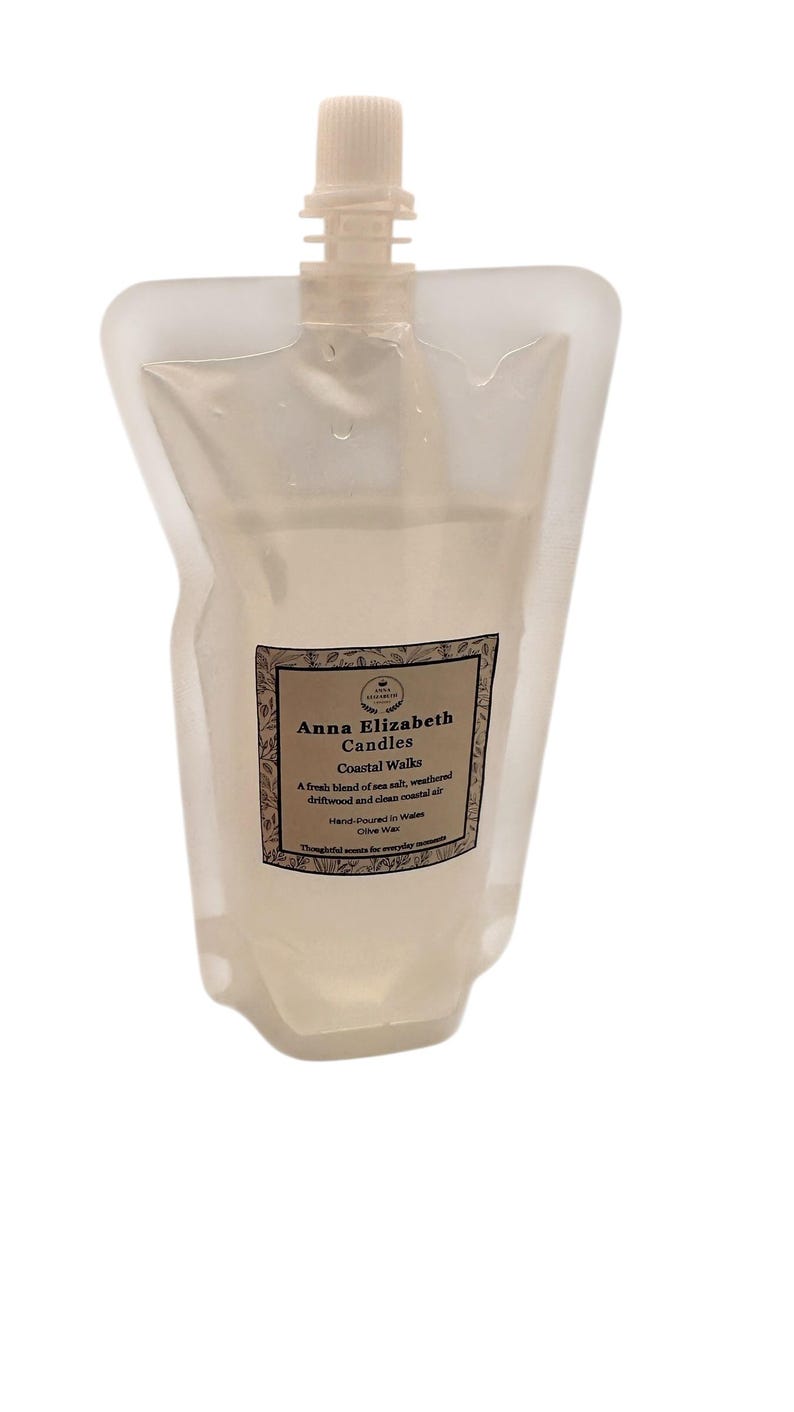 May include: A clear, flexible pouch with a white cap, containing a liquid. The label reads "Anna Elizabeth Candles Coastal Walks" with a description of the scent. The product is hand-poured in Wales and made with olive wax.