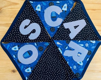 May include: A set of six blue and black fabric pennants with white stars and a space theme. Each pennant has a letter of the word "SOAR" printed in white on it.