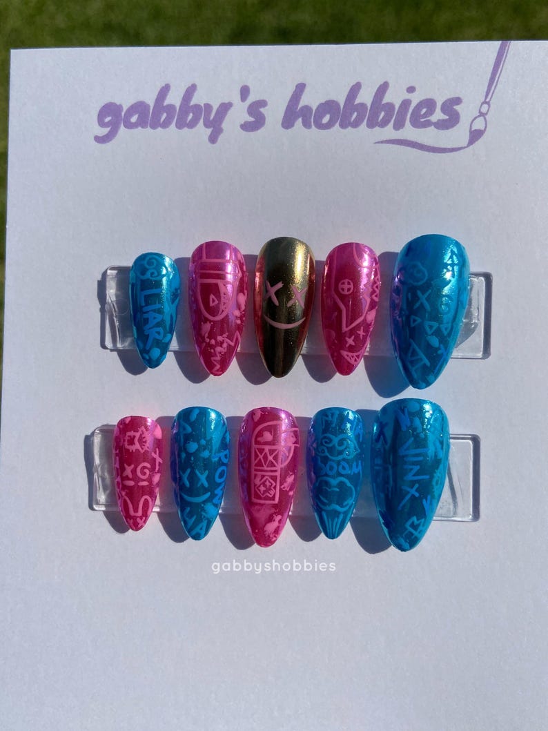 May include: Jinx nails Arcane nails Jinx inspured nails arcane inspired nails league of legends nails Gabby's Hobbies press-on nails. Ten pink and blue iridescent nails with etched designs. Designs include doodles, x's, smiley faces, and other abstract patterns.  Gold accent nail.  'Gabby's Hobbies' text is visible on the display card.