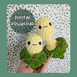 Puede incluir: Dos peluches de maíz tejidos a crochet con cáscaras verdes tejidas a crochet. Los peluches de maíz tienen hilo amarillo y ojos negros. Los peluches se sostienen en una mano.