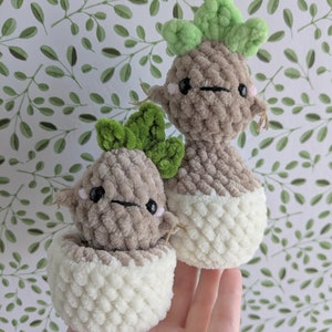 May include: Two crocheted plush toys shaped like potted plants. The plants are brown with green leaves and have cute faces. The pots are white.