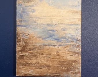 Op de afbeelding: Een abstract schilderij van een strandscène. Het kunstwerk heeft een textuur met lagen bruine, beige, blauwe en witte verf. Het onderste deel toont het zand, terwijl de bovenkant een lucht en oceaan suggereert.