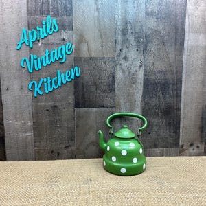May include: A green vintage teapot with white polka dots and a matching handle. The teapot is set against a rustic wooden background with the text "Aprils Vintage Kitchen" in turquoise script.