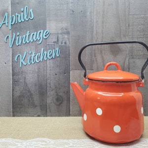 May include: An orange vintage enamel teapot with white polka dots and a black handle. The teapot has a lid and a spout. The text "Aprils Vintage Kitchen" is in the background.