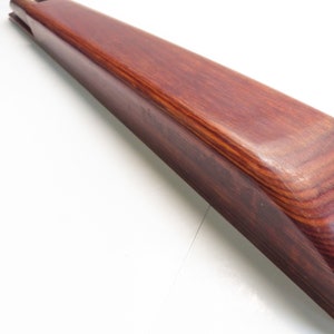 May include: A long, curved wooden object with a rich, reddish-brown hue. The wood grain is visible, and the surface appears smooth and polished. The object has a rounded edge and a groove at one end. The item is likely a decorative or functional piece.