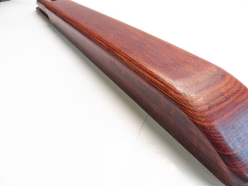 May include: A long, curved wooden object with a rich, reddish-brown hue. The wood grain is visible, and the surface appears smooth and polished. The object has a rounded edge and a groove at one end. The item is likely a decorative or functional piece.