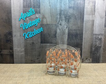 May include: A set of six vintage drinking glasses with orange polka dots, held in a white metal rack. The glasses are clear and cylindrical. The background includes the text "Aprils Vintage Kitchen" in turquoise.