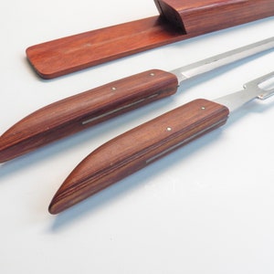 May include: A carving set with a knife and fork, featuring wooden handles and stainless steel blades. The handles are a rich, reddish-brown color, and the set includes a matching wooden storage case.