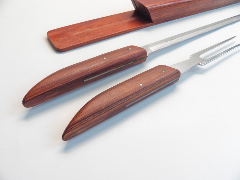 May include: A carving set with a knife and fork, featuring wooden handles and stainless steel blades. The handles are a rich, reddish-brown color, and the set includes a matching wooden storage case.