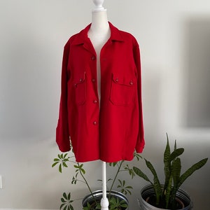 May include: A red wool shirt jacket with a button-up front and two large pockets on the chest.