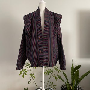 May include: A striped bomber jacket with a dark background and colourful stripes in shades of pink, green, and yellow. The jacket has a stand-up collar and a button closure.