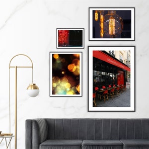 Può includere: Una collezione di stampe artistiche incorniciate esposte su una parete bianca. Le stampe raffigurano una lampadina, un caffè con tenda rossa ed effetti bokeh astratti. Le cornici sono nere.