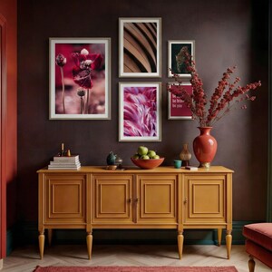 Può includere: Una credenza giallo senape con opere d'arte incorniciate e un vaso rosso pieno di rami. L'arte comprende stampe floreali e astratte. Una ciotola di mele verdi è posizionata sulla credenza, insieme a oggetti decorativi. Il muro è di colore bordeaux scuro.