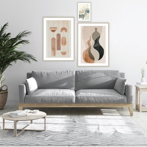 May include: A living room scene featuring a gray sofa, a round coffee table, and a patterned rug. The wall displays three framed abstract art prints in neutral tones. A potted palm tree in a woven basket and a side table with a lamp complete the decor.