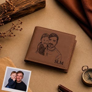 K&ouml;nnte beinhalten: Eine braune Lederbrieftasche mit einer lasergravierten Illustration einer Person, die ein Kind h&auml;lt. Die Gravur zeigt die Gesichtsz&uuml;ge beider Personen, und die Buchstaben SLM sind in der unteren rechten Ecke der Brieftasche eingraviert.