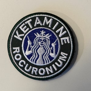 May include: A green and white embroidered patch with the text "KETAMINE ROCURONIUM" in a circle around a blue and white stylised mermaid with a crown.