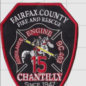 May include: A black embroidered patch with a red border featuring the text FAIRFAX COUNTY FIRE AND RESCUE, ENGINE 15, CHANTILLY, SINCE 1947, AMBULANCE, and BC 403. The center depicts a knight on a horse holding a yellow lance with red accents.
