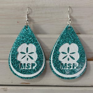 Puede incluir: Pendientes de lágrima con purpurina turquesa, diseño de dólar de arena blanco y las letras "MSP". Los pendientes tienen ganchos plateados. Un accesorio único.