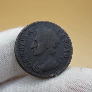 May include: A dark brown antique coin with a profile of a person facing right. The coin has the inscription "CAROLVS A CAROLO" around the edge. The coin is slightly worn, showing signs of age and use.