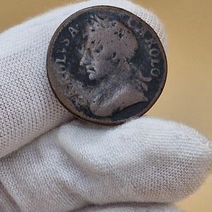 May include: A silver coin with a portrait of a man on one side and the text "CAROLUS" around the edge.