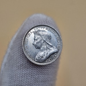 Może przedstawiać: Srebrna moneta z profilem kobiety w koronie i draperii. Krawędź monety zawiera napis „VICTORIA DEI GRA BRITT REGINA FID DEF IND IMP.”