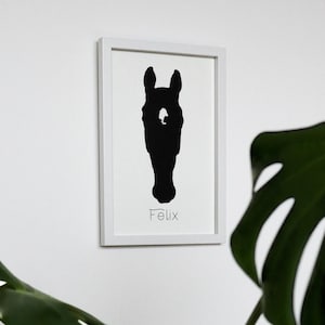 Könnte beinhalten: Ein gerahmter Druck mit einer schwarzen Silhouette eines Pferdekopfes. Der Name "Felix" ist in einer Schrift darunter geschrieben. Das Kunstwerk befindet sich vor einem weißen Hintergrund in einem weißen Rahmen, was einen minimalistischen Stil erzeugt.