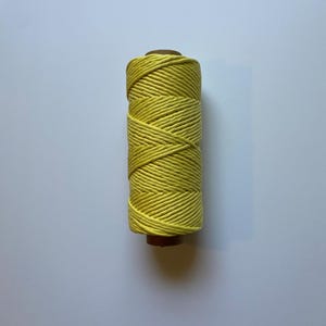 May include: A spool of bright yellow cotton thread. The thread is tightly wound around a brown cardboard core. The color is a vibrant, sunny yellow, and the texture of the thread appears smooth. Ideal for crafting and sewing projects.