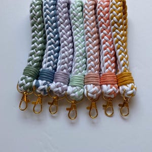May include: Set of seven braided keychains in various colors, including green, blue, purple, light green, pink, orange, and yellow. Each keychain has a gold metal key ring.