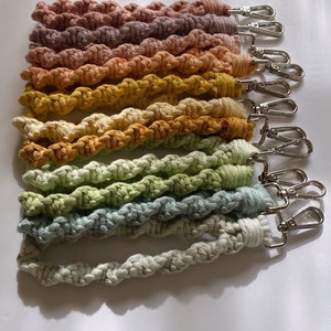 May include: A set of ten colorful crocheted keychains with silver clasps. The keychains are made of a thick, twisted cord and are arranged in a rainbow pattern.