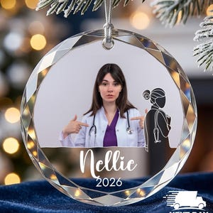 May include: A circular faceted glass ornament featuring a photograph of a person in a white medical coat and purple shirt, a black silhouette of a medical professional, and the white text Nellic 2026 printed on the surface with a silver cord.