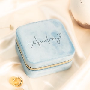 May include: A light blue velvet jewelry box with a gold zipper. The box is personalized with the name "Audrey" and a small heart.