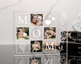 May include: A clear acrylic photo frame with a grid of nine squares. Each square contains a photo of a family. The frame is engraved with the word "MOM" and the text "Tom & Alexis". The frame is sitting on a stack of books with a wooden heart-shaped sign that reads "The secret ingredient is always love" and "HOME my happy place".