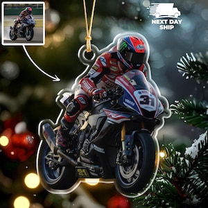May include: A motorcycle racing ornament featuring a rider on a black and blue Yamaha R1 motorcycle. The rider wears a red and white racing suit and a helmet with a colorful design. The ornament has a gold string for hanging.