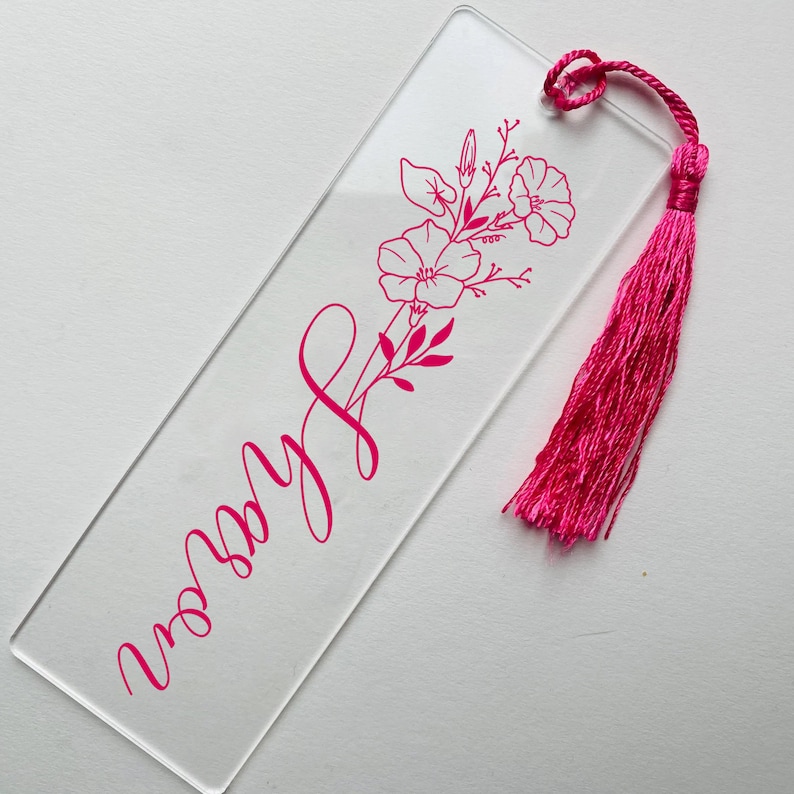 May include: A clear acrylic bookmark with a pink floral design and the word "worry" written in cursive. The bookmark has a pink tassel.