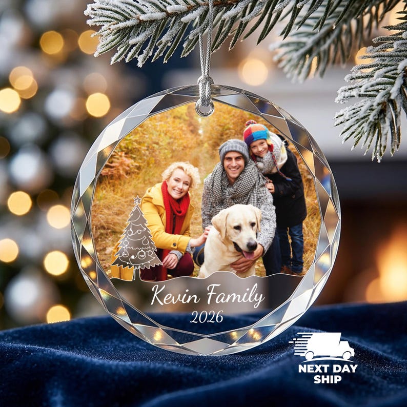 May include: A round, faceted glass Christmas ornament featuring a printed photograph of a family with a dog in an autumn forest. The ornament includes a white graphic of a Christmas tree, the text "Kevin Family" and "2026" in white script.