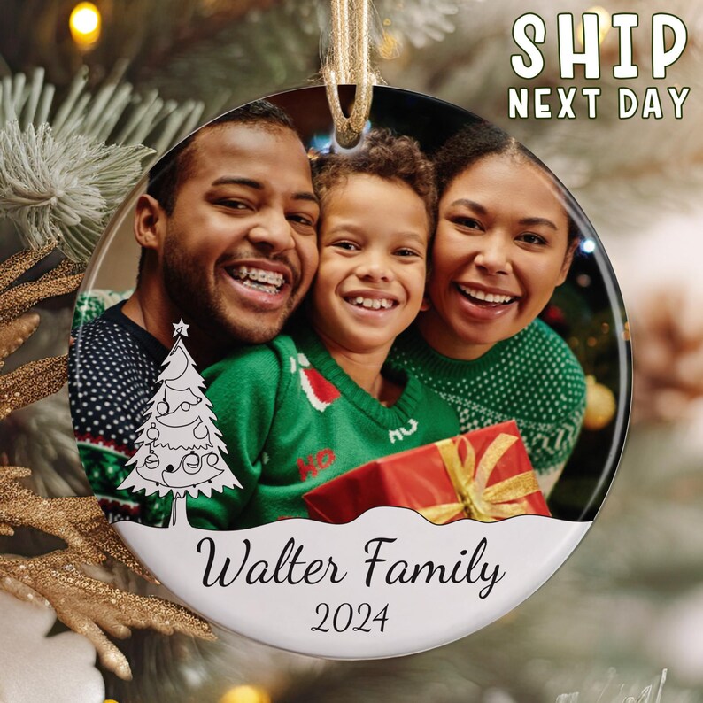 May include: A round ceramic Christmas ornament featuring a printed photograph of a family of three smiling. The ornament displays a white graphic of a Christmas tree, the text Walter Family, and the year 2024 printed in black script font.
