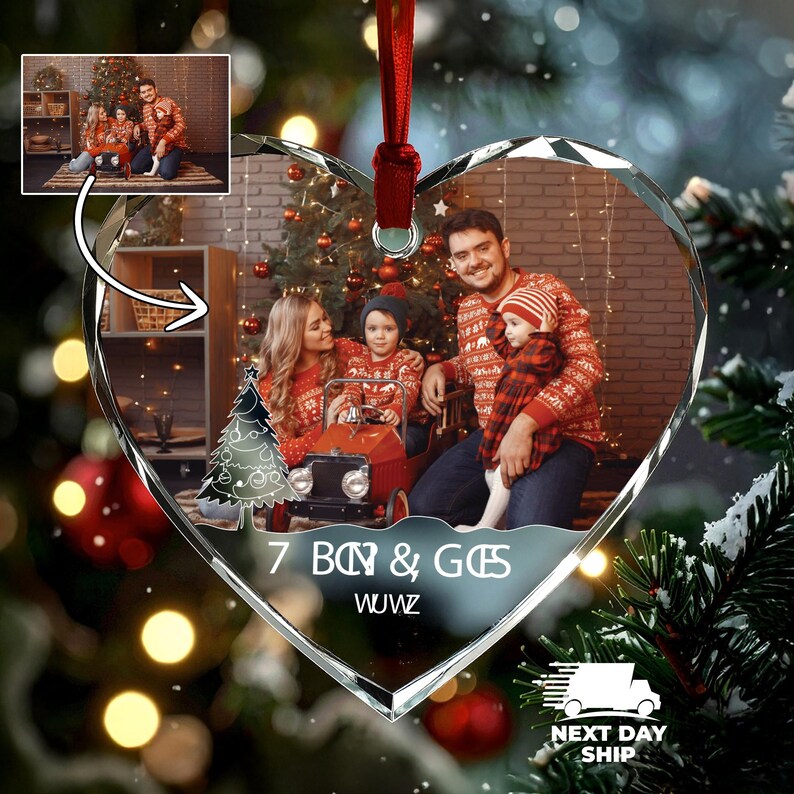 May include: A heart-shaped glass Christmas ornament featuring a printed photograph of a family sitting in front of a decorated tree. The ornament includes a white graphic of a Christmas tree and the text 7 BOY & GIES WUWZ, suspended by a red ribbon.