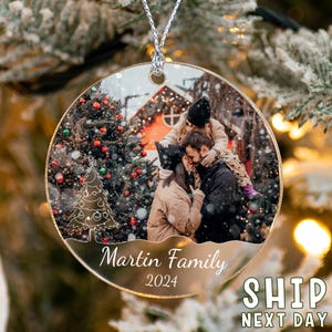 May include: A circular clear acrylic Christmas ornament featuring a printed photograph of a family in a snowy outdoor setting. The ornament includes a white line-art Christmas tree graphic, the text Martin Family, and the year 2024.