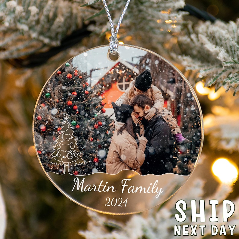 May include: A circular clear acrylic Christmas ornament featuring a printed photograph of a family in a snowy outdoor setting. The ornament includes a white line-art Christmas tree graphic, the text Martin Family, and the year 2024.