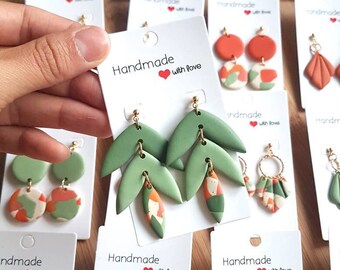 May include: A collection of handmade polymer clay earrings displayed on white cards. The earrings feature various shapes including leaves, circles, and semi-circles in shades of sage green, burnt orange, and speckled patterns with gold-toned hardware.