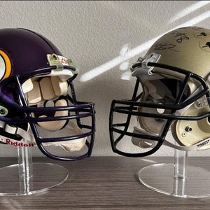 May include: Two football helmets on clear acrylic stands. The helmet on the left is purple with a yellow logo and the helmet on the right is gold with black lettering that says "UCI Knights".