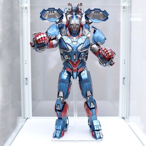 Puede incluir: Una figura de acci&oacute;n azul y roja de un robot con casco y m&uacute;ltiples armas. El robot est&aacute; de pie sobre una superficie blanca.