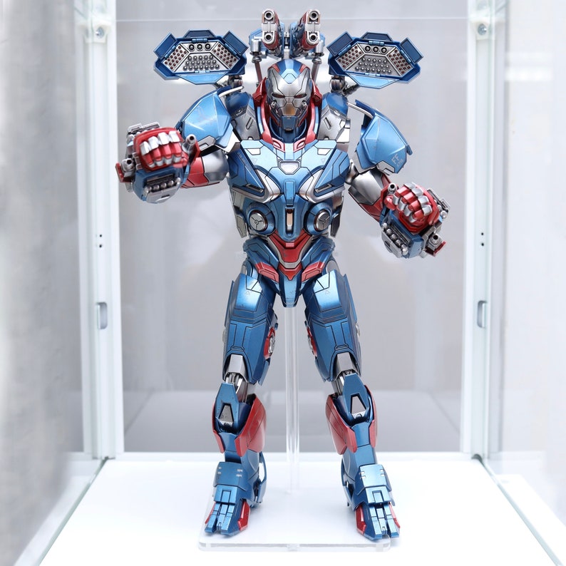 Puede incluir: Una figura de acci&oacute;n azul y roja de un robot con casco y m&uacute;ltiples armas. El robot est&aacute; de pie sobre una superficie blanca.