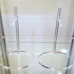 May include: Two clear acrylic display stands with round bases. The stands are designed to hold items upright.