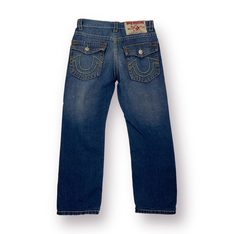 May include: A pair of blue denim jeans with a yellow stitched True Religion logo on the back pockets.